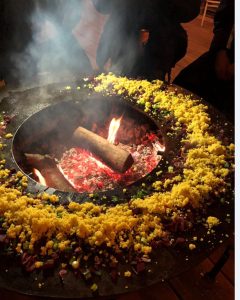 Auf einer Kochplatte um ein offenes Feuer ist eine Speise zum ausgelegt.