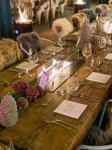 Blick auf eine winterlich gedeckte Tafel mit Tannenzapfen als Dekoration und einem kleinen Tischfeuer.