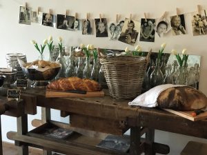 Blick auf ein Buffet auf einer alten Werkbank. Schwarz-weiß Fotografien über einem Buffet mit Backwaren und Blumevasen.