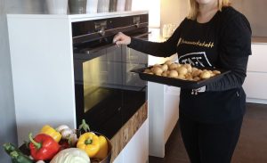 Eine Mitarbeiterin der Genusswerkstatt ist im Begriff ein Blech Kartoffeln in den Ofen zu schieben.